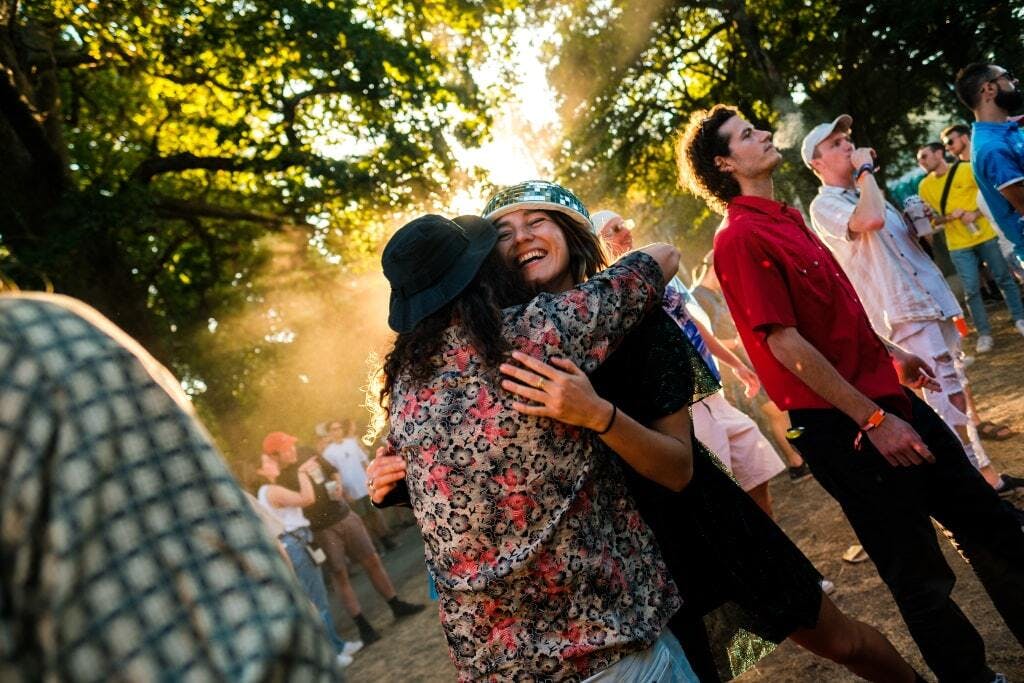 Two people hugging at a music festival surrounded by trees. 