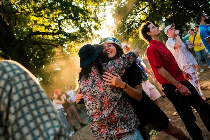 Two people hugging at a music festival surrounded by trees. 