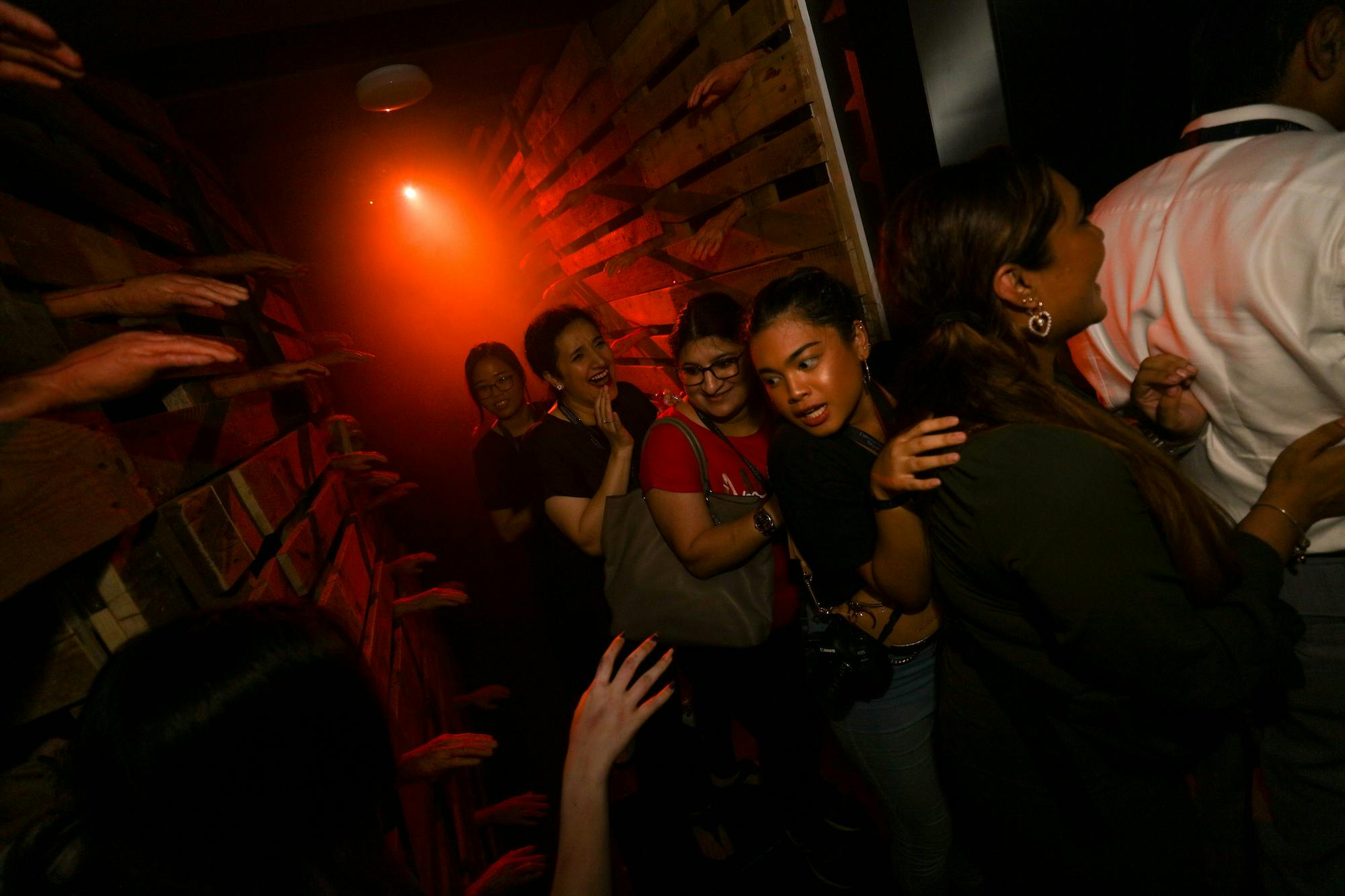 People in a spooky corridor washed in red lighting at Halloween Horror Nights 10 at Universal Studio Singapore. A person in costume scares them. 