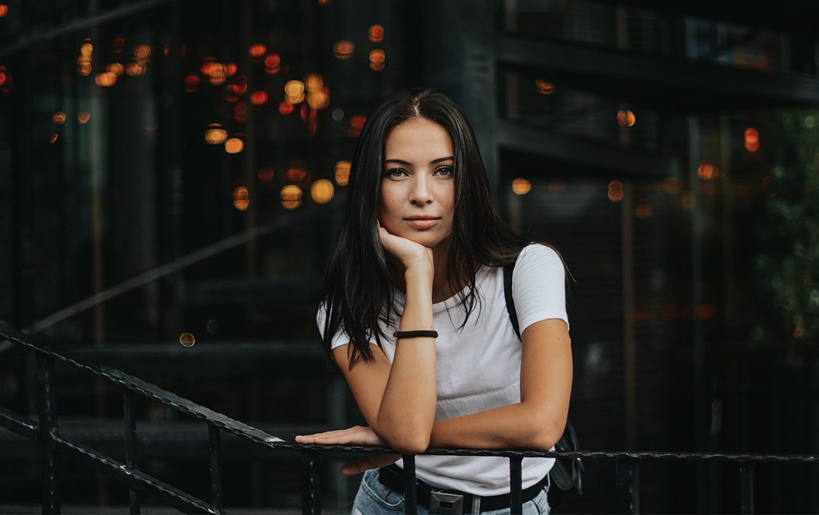 a woman rest her head on her hands, while leaning against a balcony railing.
