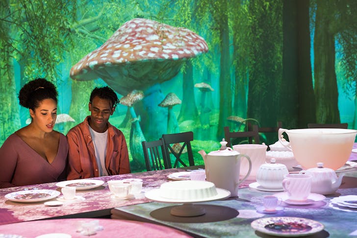 Two people sitting at the Mad Hatter's Tea Party with a large mushroom behind them.