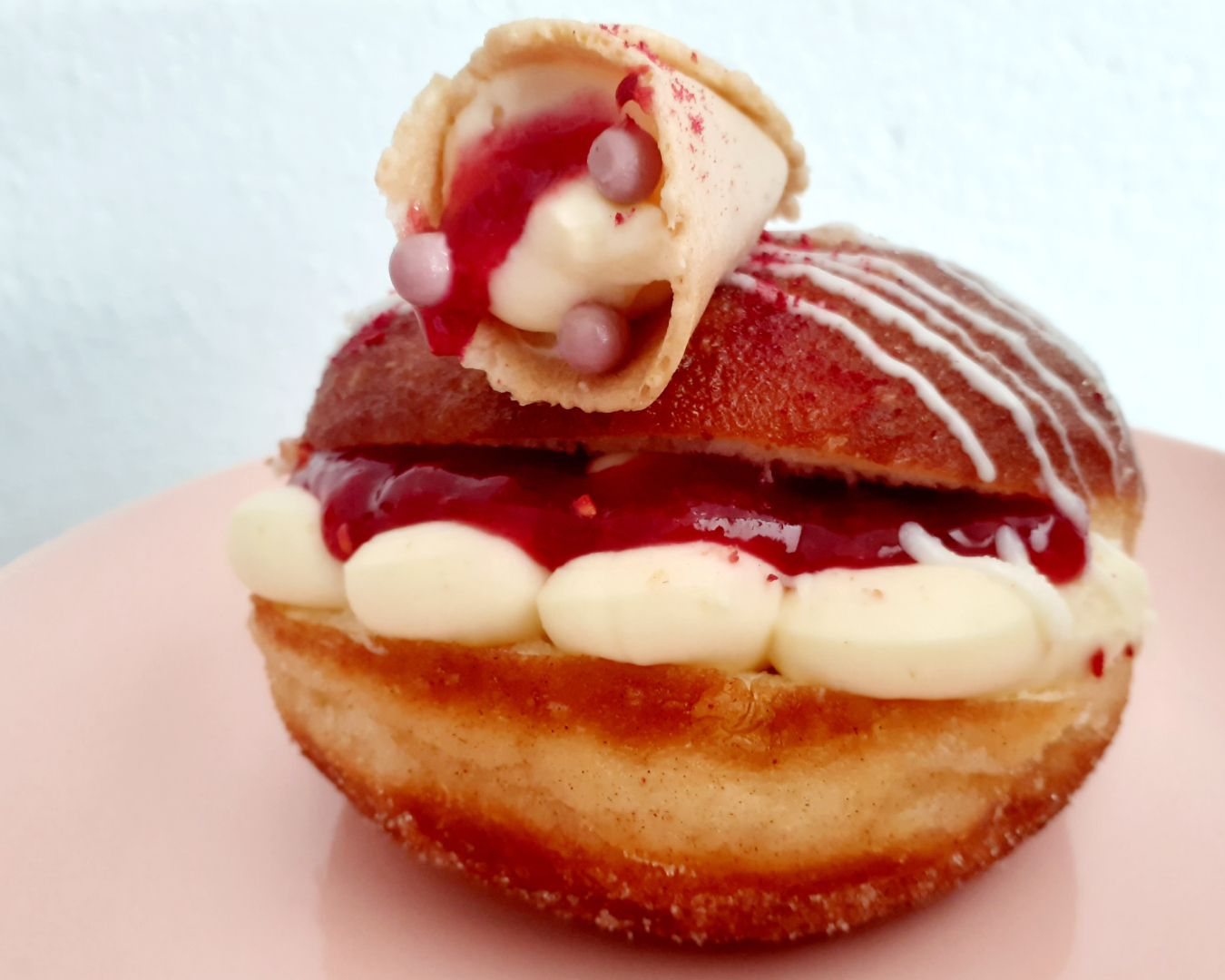 A delicious looking doughnut filled with cream and berry sauce, topped with a tuile containing more cream and berry sauce!
