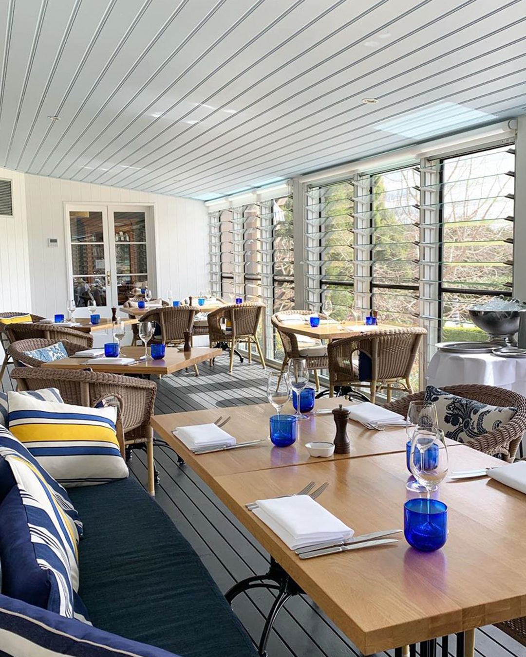 A spacious dining area on the verandah with nautical-style soft furnishings and blue glasses.