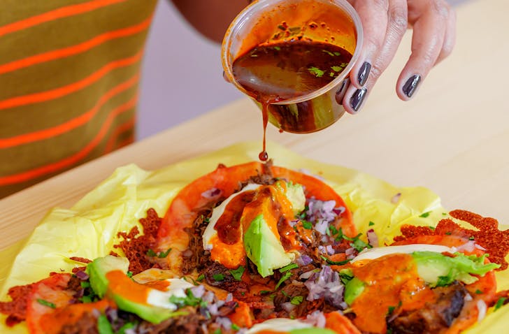 Armelle pours sauce over a plate of four birria tacos. 