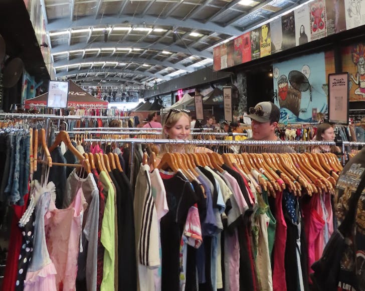 Young adult caucasian male and female flick through vintage clothing racks in a big warehouse setting.