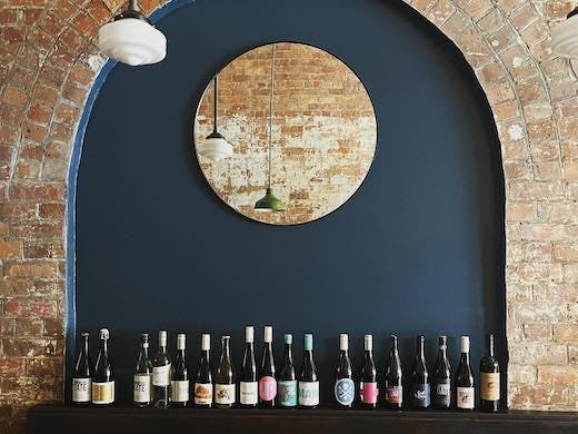 Several bottles of wine are lined up against a heritage brick wall with an elegant pendant light above.