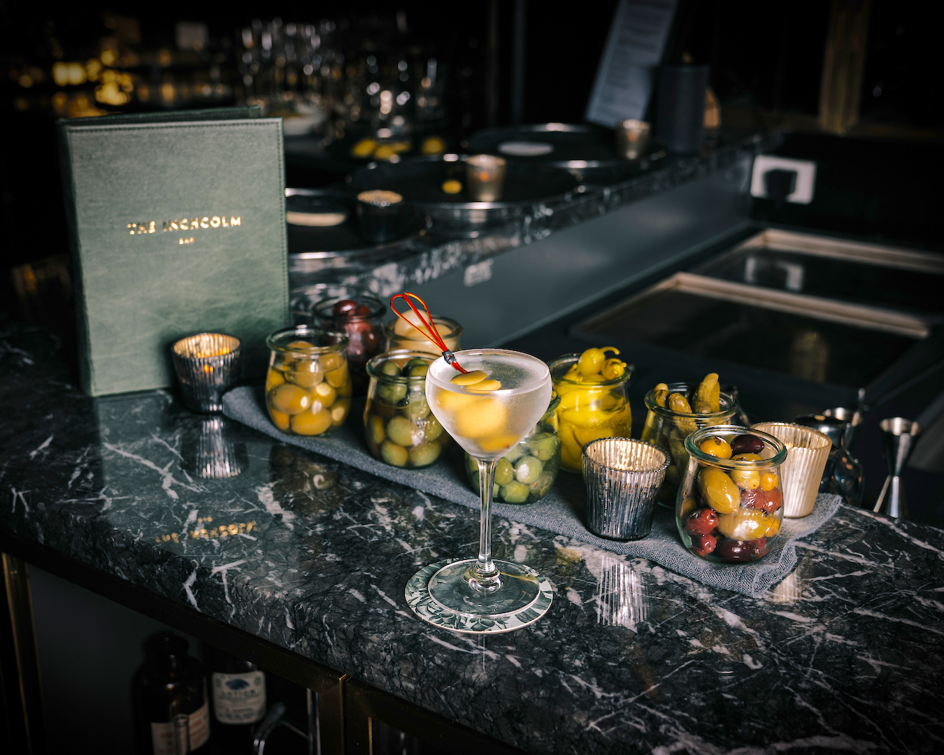 A dark marble bar top covered with martini ingredients including olives.