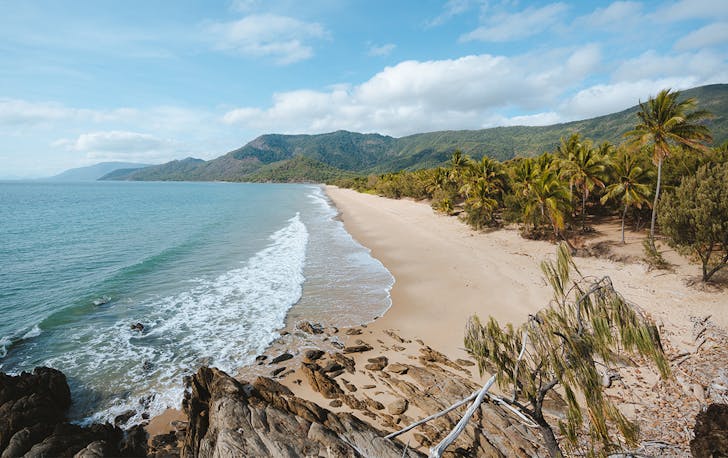 white sand, framed by palm trees and mountains, meets a glittering blue ocean.