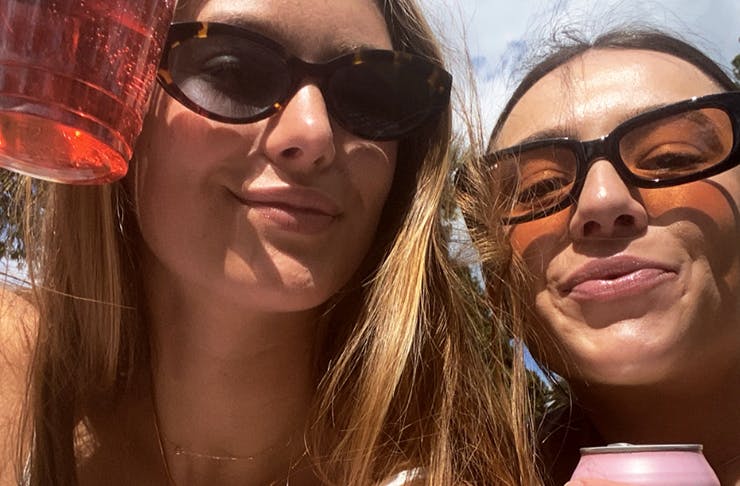 Two girls with drinks in their hands looking at the camera. 