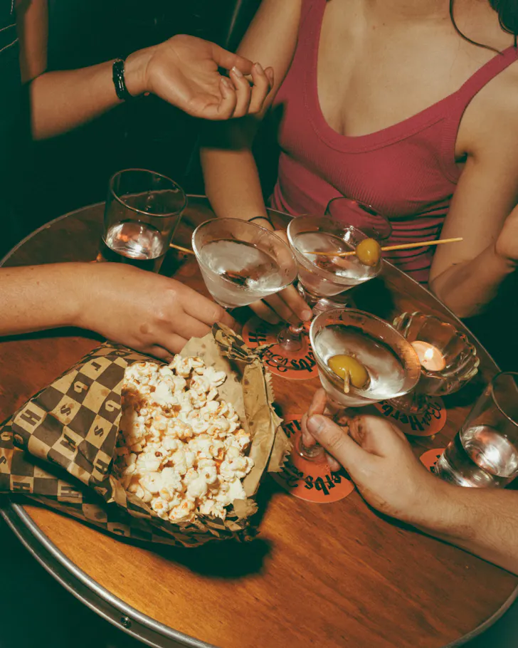 A group of friends at a bar table with popcorn and cocktails.