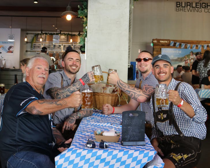 Four lederhosen clad men of varying ages sit around a table clinking steins of beer in the Burleigh Brewing Co taproom