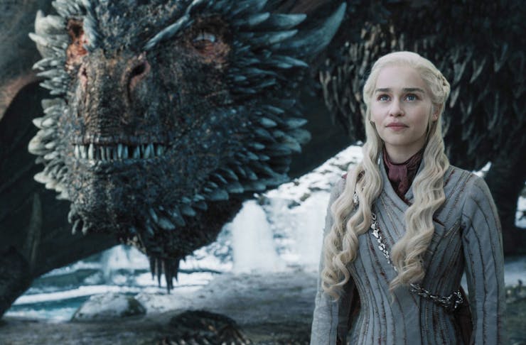 daenerys on set of Game Of Thrones stands in front of a dragon.