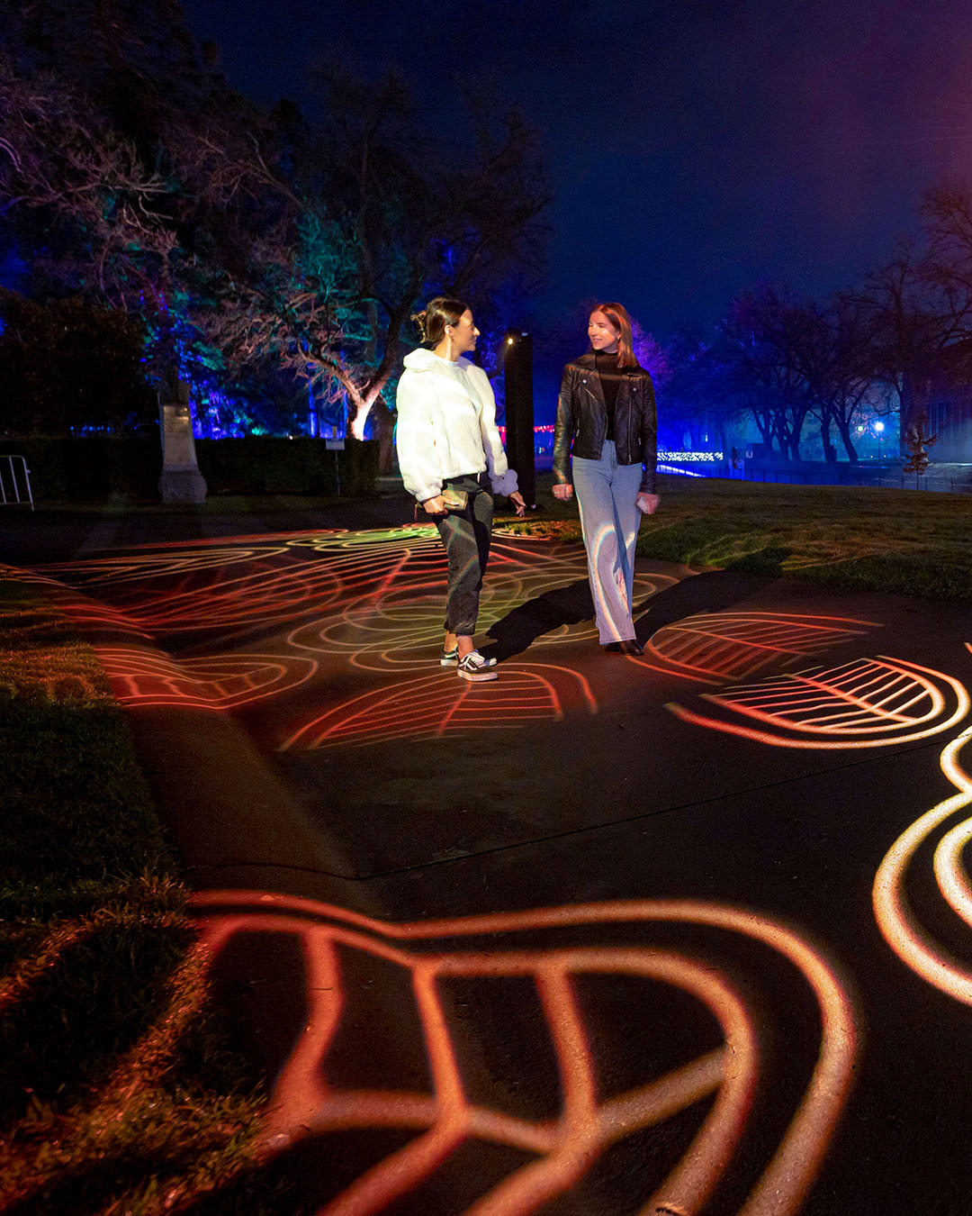 Two people walking on a park path, illuminated with designs at GLOW Bendigo. 