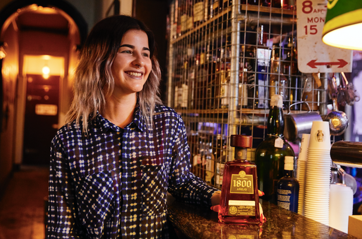 Tequila specialist Hayley Dixon at a bar with a plaid shirt on and holding a bottle of Jose Cuervo Tequila. 