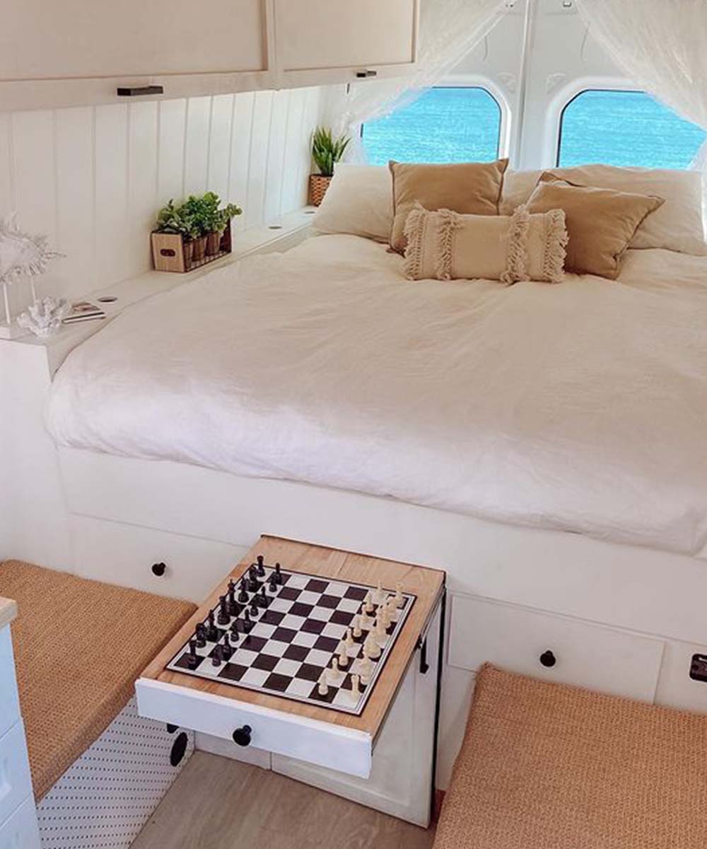 a white bed and chess set feature in the back of the Happy Camper Van
