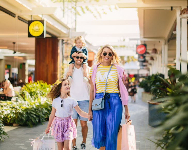 Family consisting of father, mother, daughter and son walking between the eateries at Harbour Town, smiling and carrying shopping bags