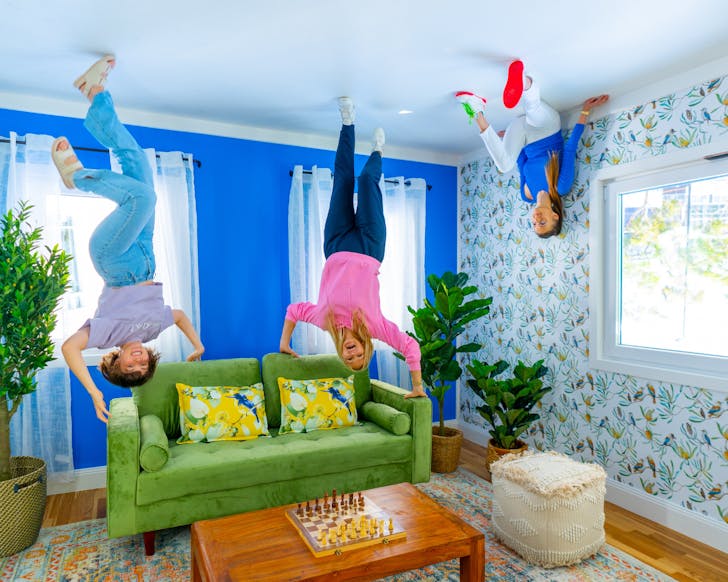 One woman and two children appearing to hang from the ceiling above a living room with a green couch