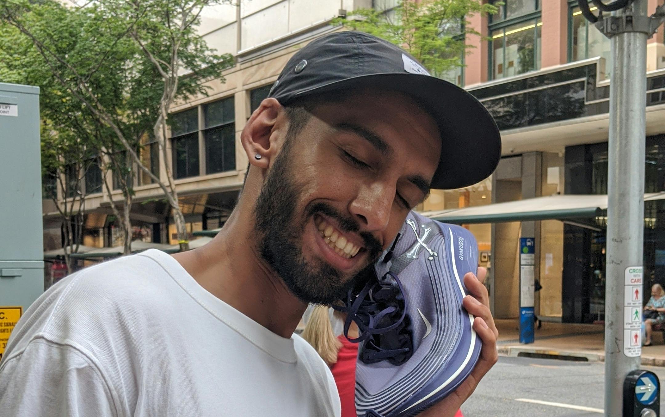 A person with a beard holding a running shoe as if it's a phone. 