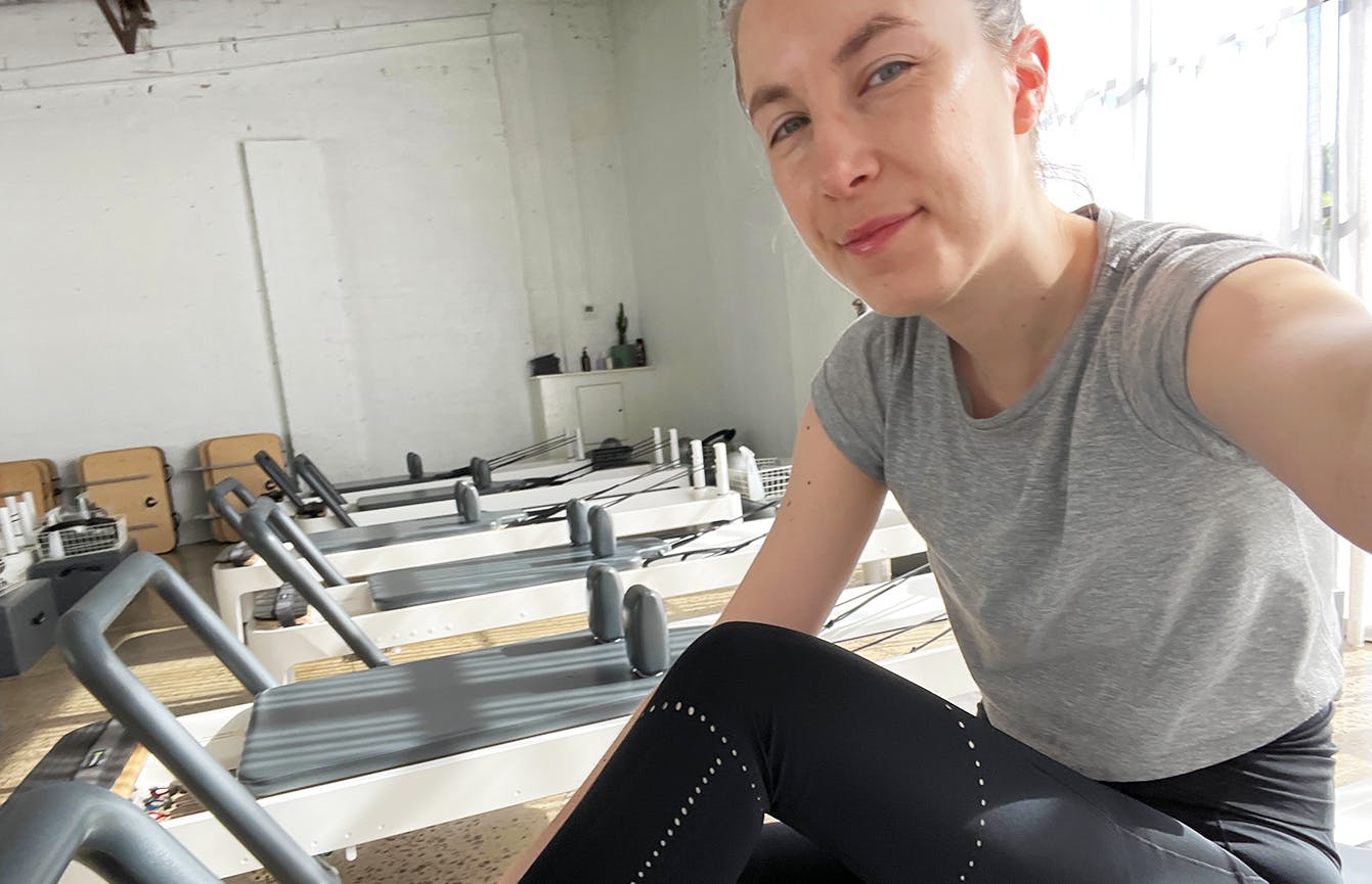 A person sitting on a pilates reformer in a brightly lit studio