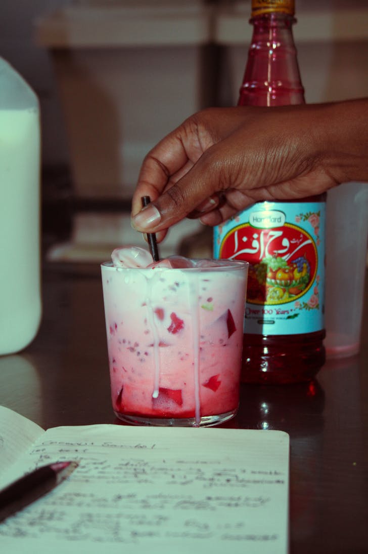 a hand mixing a bright drink on a stainless steel surface