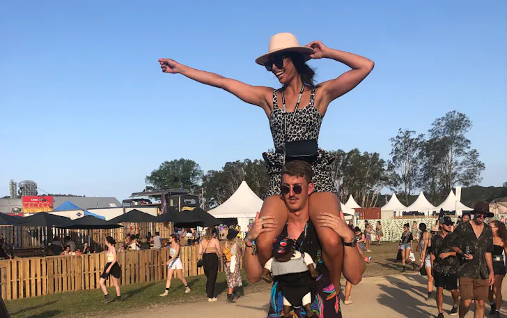 One person on another's shoulders with the tent tops of a music festival in the background 
