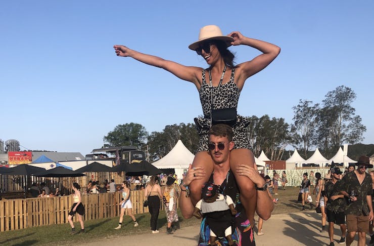 One person on another's shoulders with the tent tops of a music festival in the background 