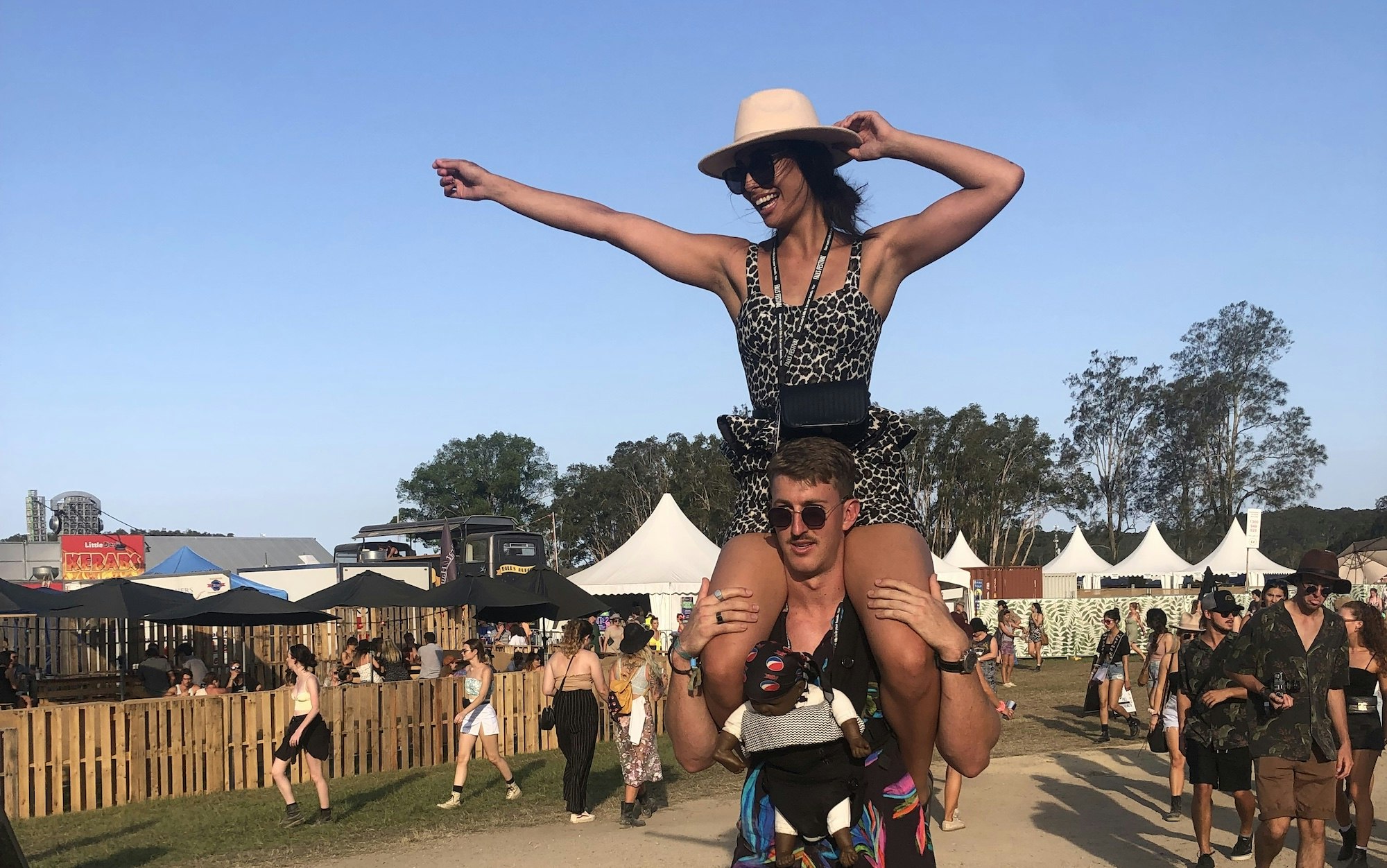 One person on another's shoulders with the tent tops of a music festival in the background 