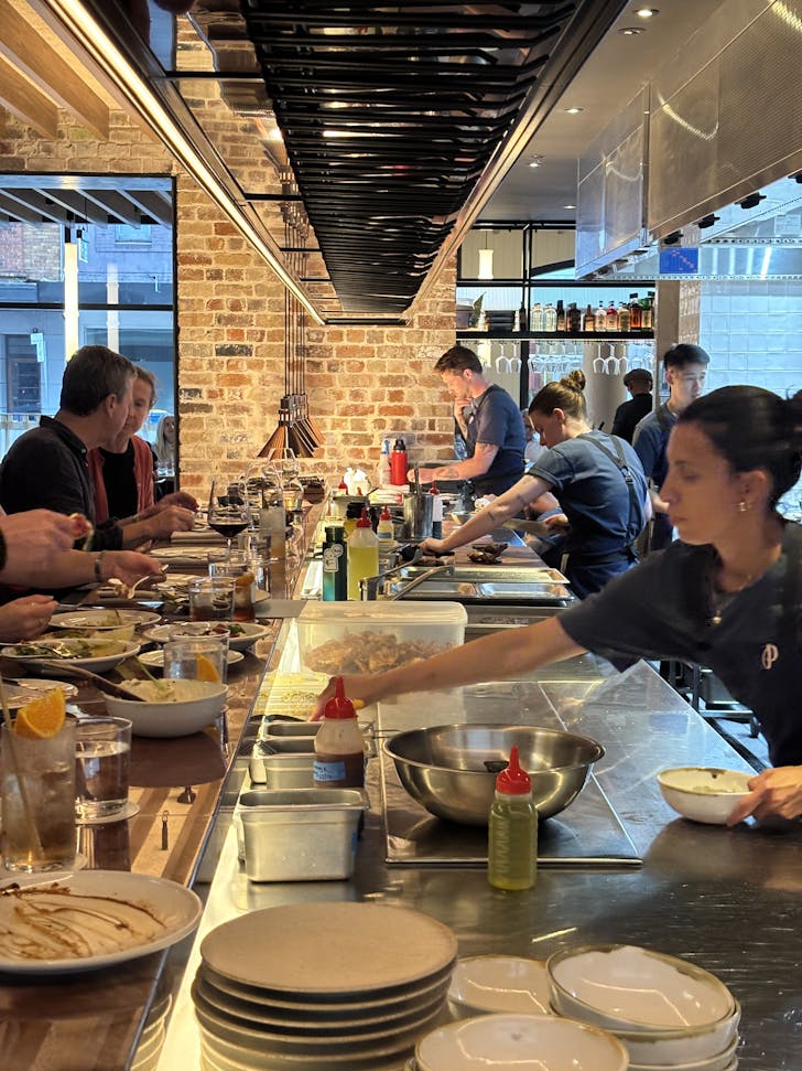 people sitting at a kitchen bar in a restaurant with chef's cooking on the other side