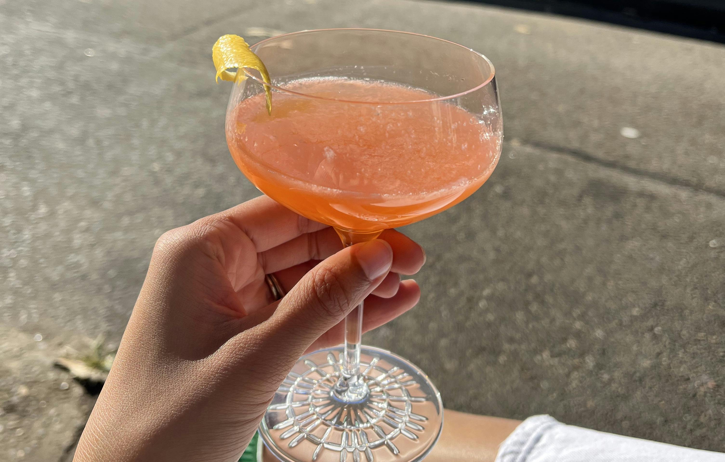 A hand holding a cocktail with a footpath and road in the background