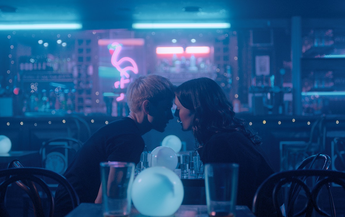 two young women hang their heads close together over a table in a diner. 