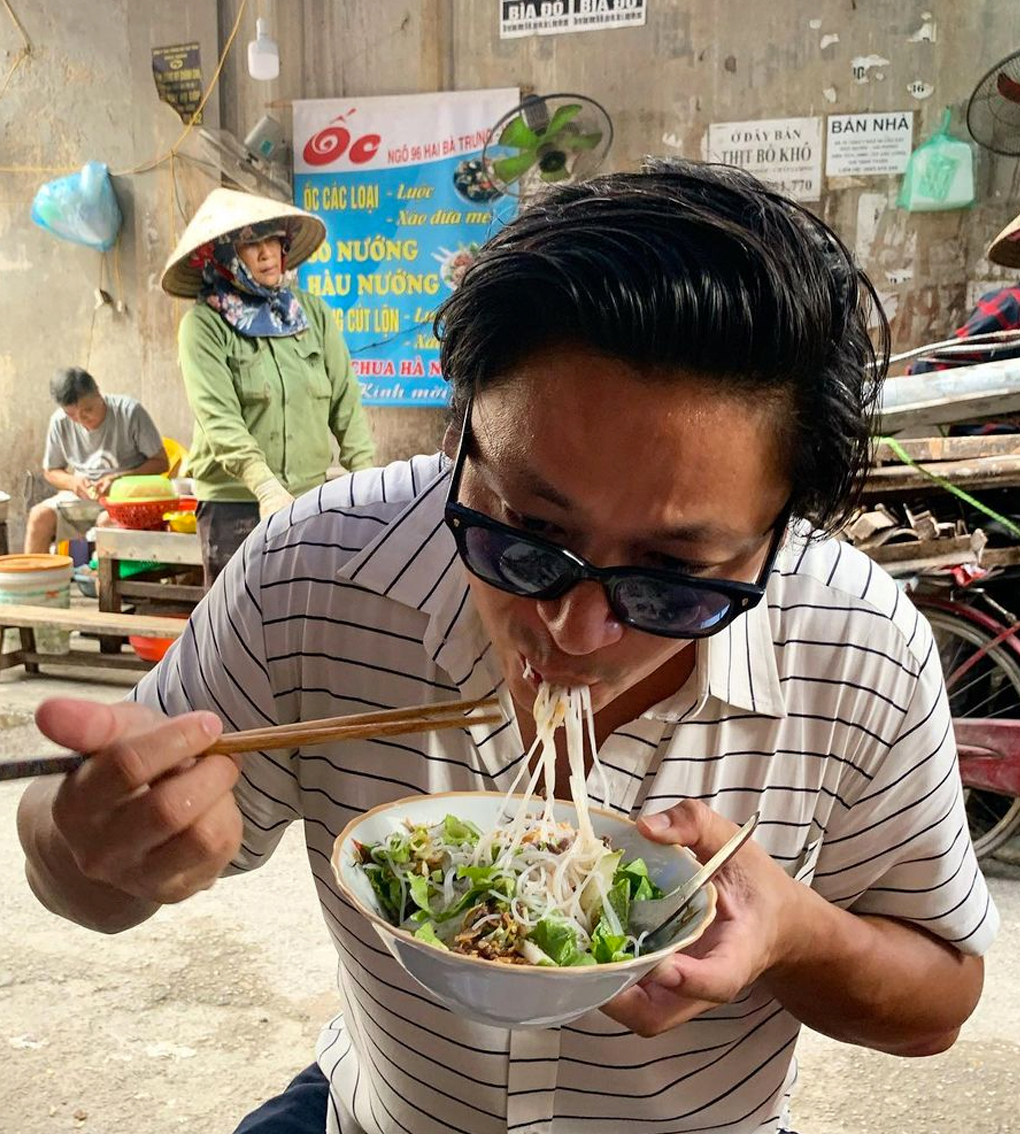 man slurping on bowl of noodles in street