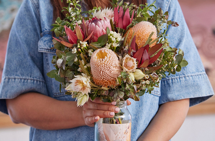 A person in a denim jacket holding a jar full of native Australian flowers from one of the best flower delivery Melbourne services, LVLY