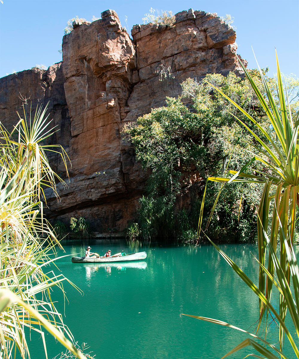 a canoe paddling along a body of blue water amongst huge red rock faces