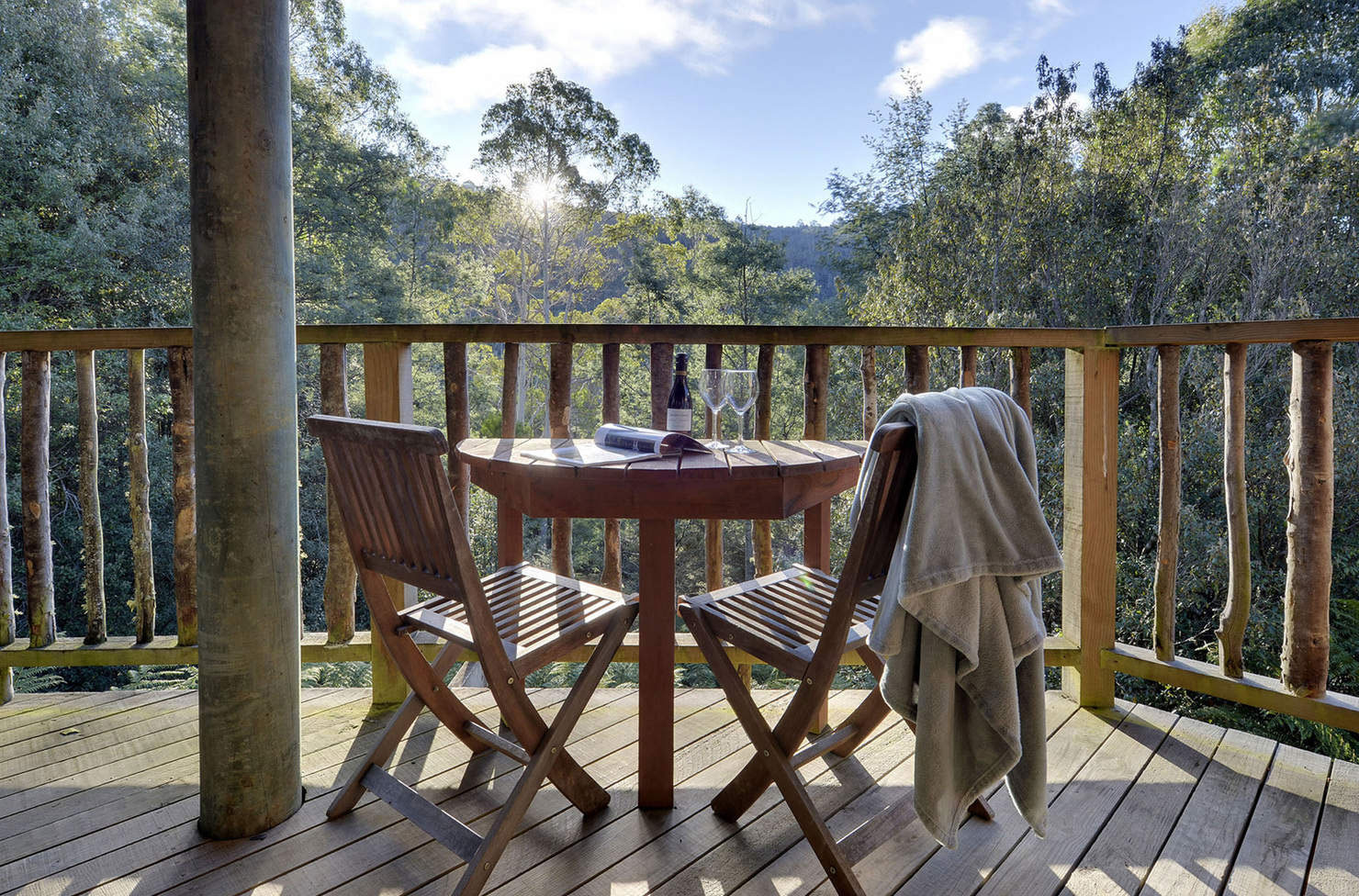 a table and two chairs on a wooden balcony overlooking the wilderness