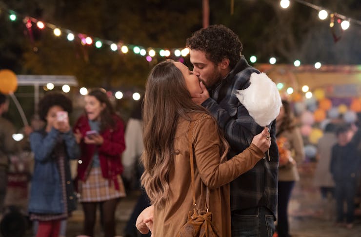 two people kissing at a fair under fairy lights, one is holding cotton candy