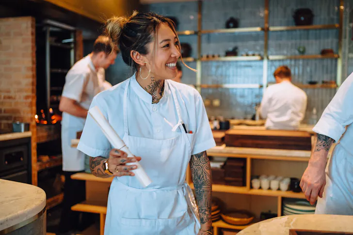 a chef with their hair tied back and smiling in a restaurant