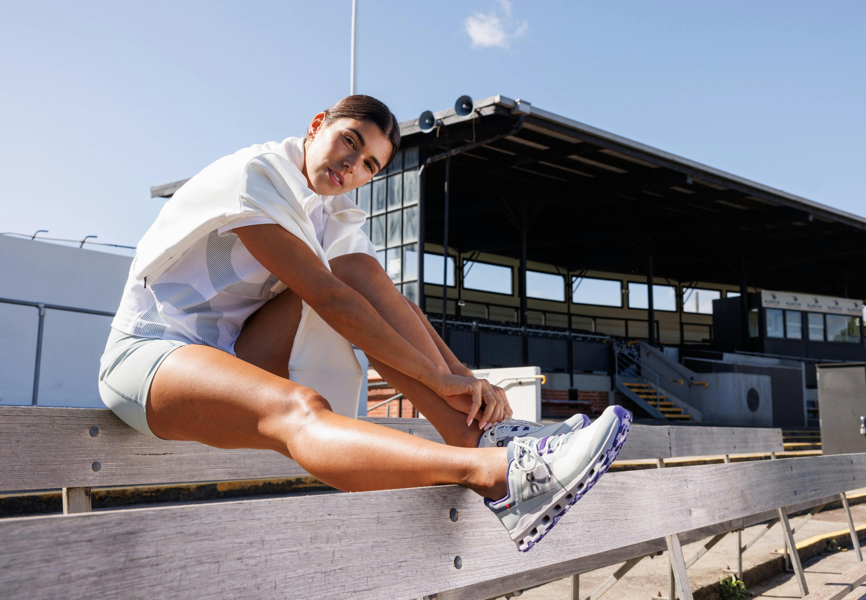 Women sitting in a stadium in gym gear and running shoes.