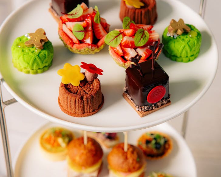 Mini multi-coloured high tea treats sit on a tiered white plates.