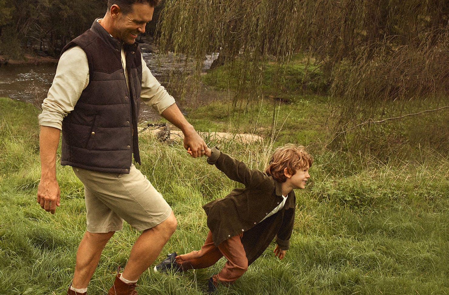 Man in a park wearing R.M.Williams with a child pulling his arm.