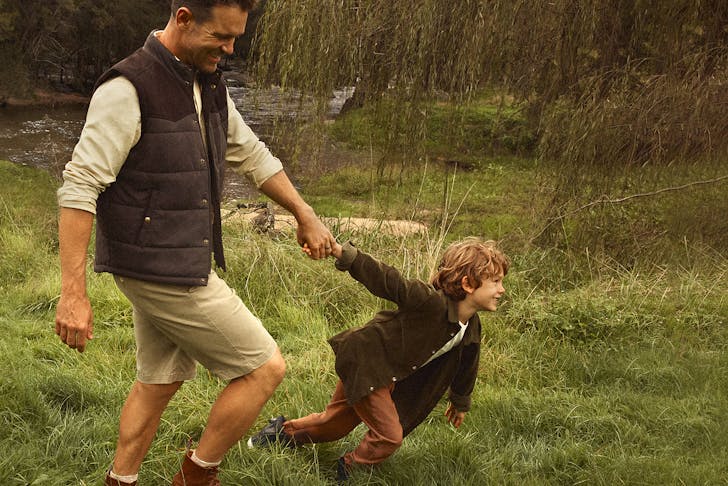 Man in a park wearing R.M.Williams with a child pulling his arm.
