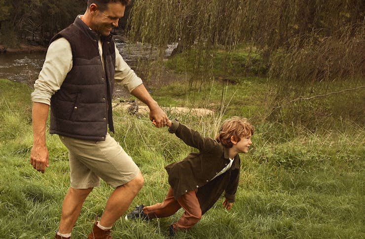 Man in a park wearing R.M.Williams with a child pulling his arm.