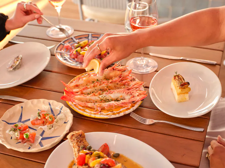 hands squeezing lemon over prawns on a plate