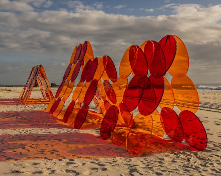 Large sculpture made up of translucent orange circles sat on the sand at Currumbin Beach