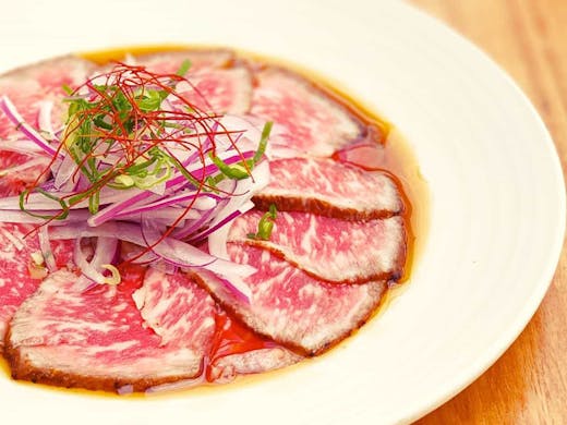 A plate of quality, thinly-sliced Wagyu beef in a shallow broth. 
