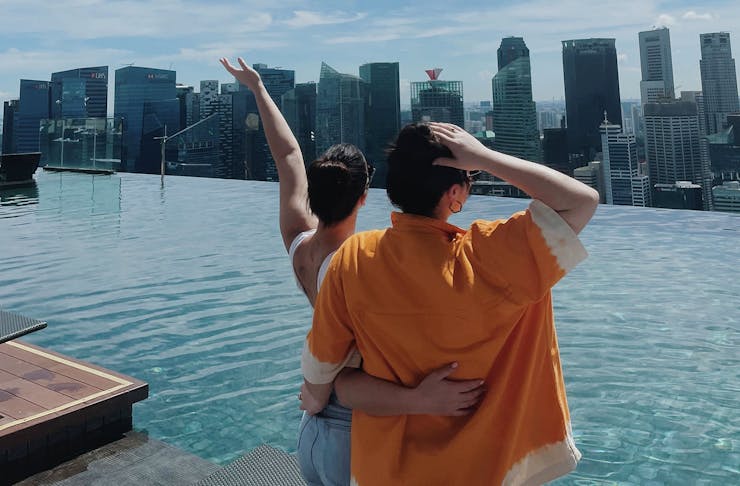 Two women standing in front of a rooftop pool overlooking Singapore.