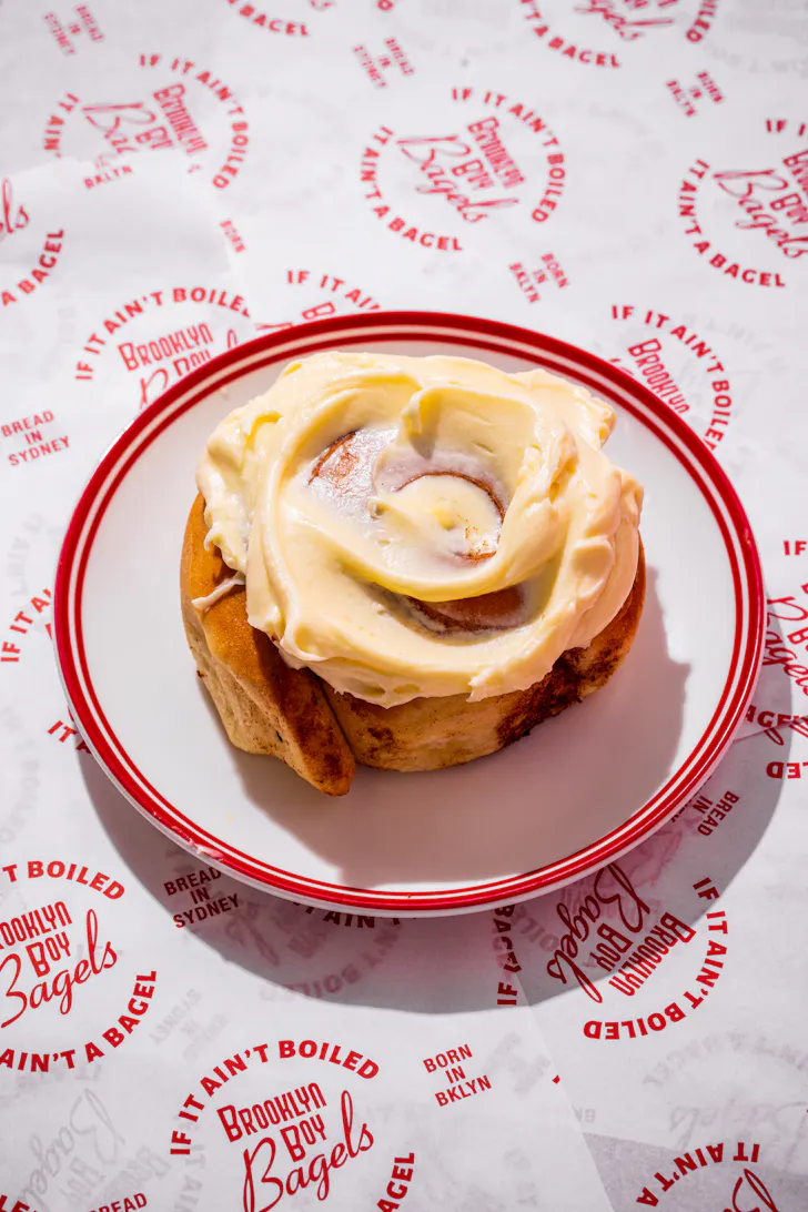 a cinnamon scroll on a plate, over branded paper that says 'brooklyn boy bagels'