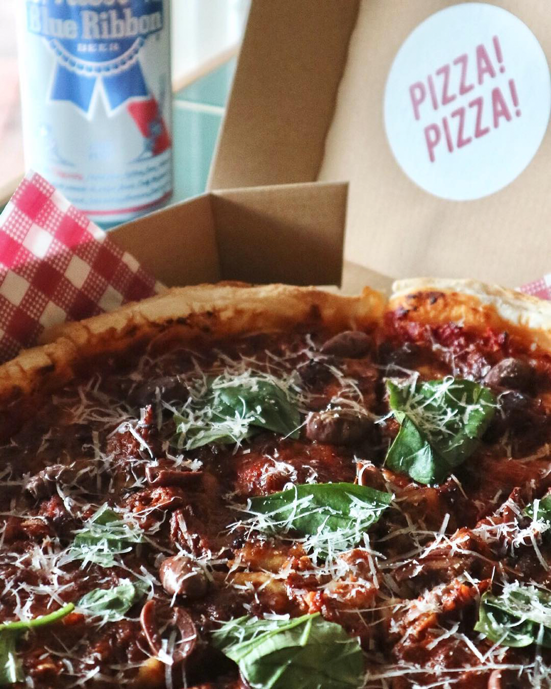 A takeaway pizza box with meaty and cheesy topppings accompanied by a Blue Ribbon beer.