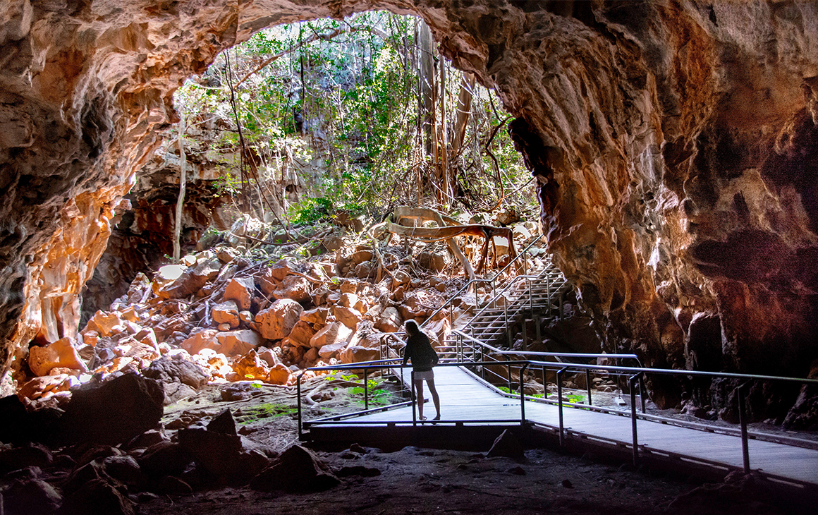 A girl standing underneath an orange lava rock cave 