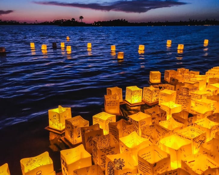 Water lanterns with hand written notes on them floating on the water at sunset.