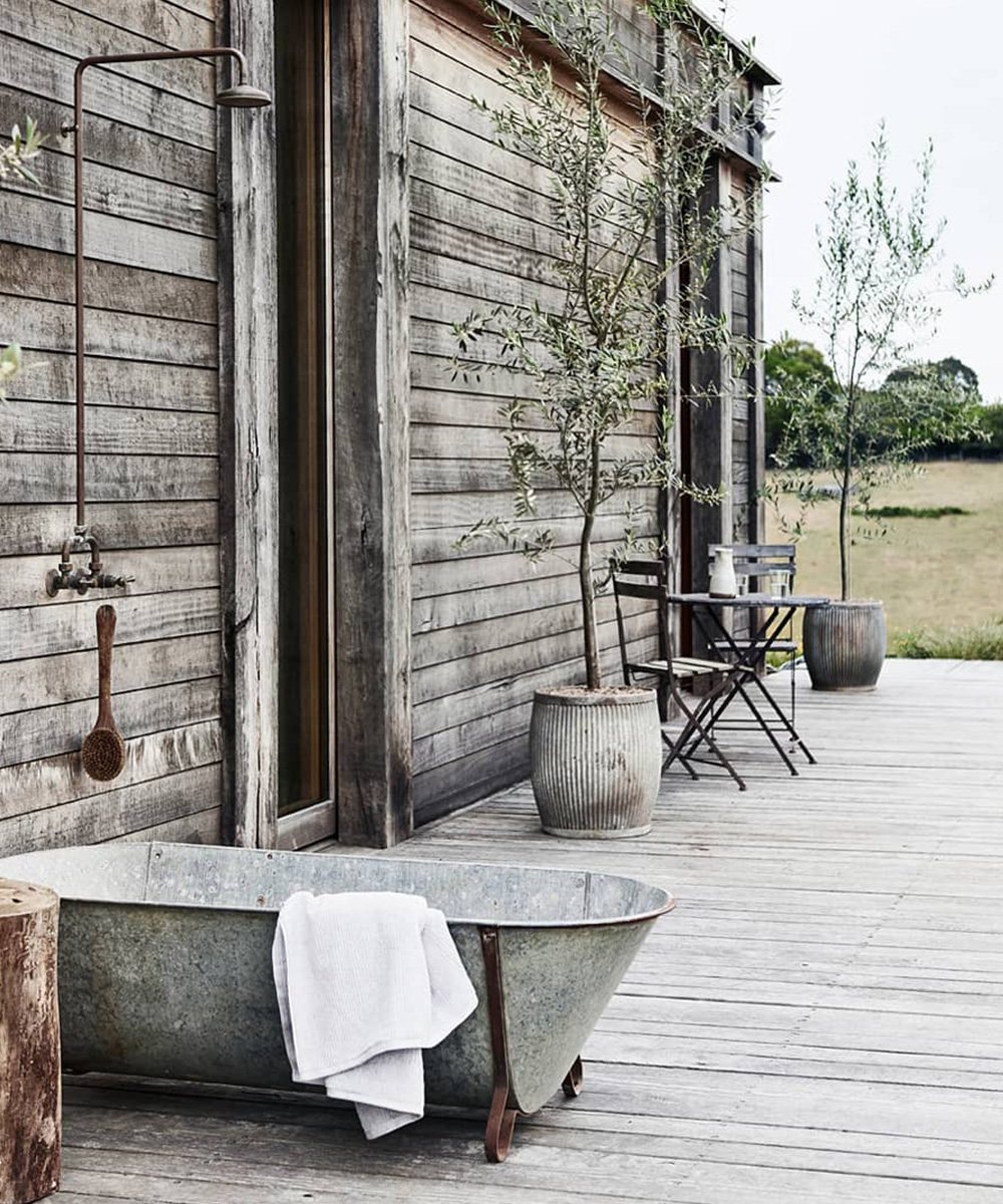 a steel freestanding tub on a wooden deck with a shower above it.